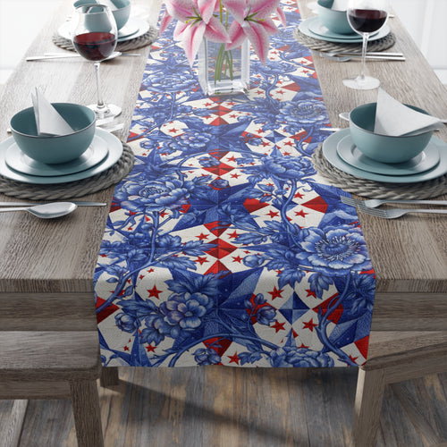 Patriotic table runner with a blue toile-inspired floral pattern layered over a red and white geometric star background, displayed on a wooden table with elegant place settings.