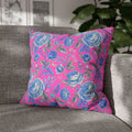 A vibrant square throw pillow with a pink and blue rose floral pattern placed on a grey textured sofa in a bright modern living room.