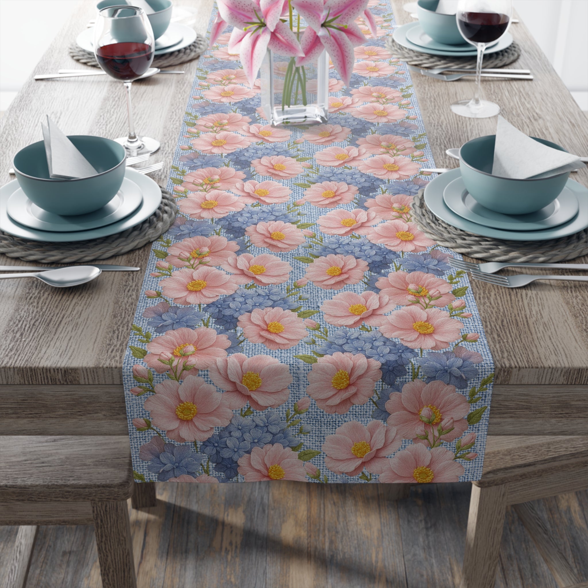 Close-up of a Blush Peony Floral Table Runner from the Soft Provence collection on a rustic wooden table with blue ceramic plates and pink lilies in a vase.