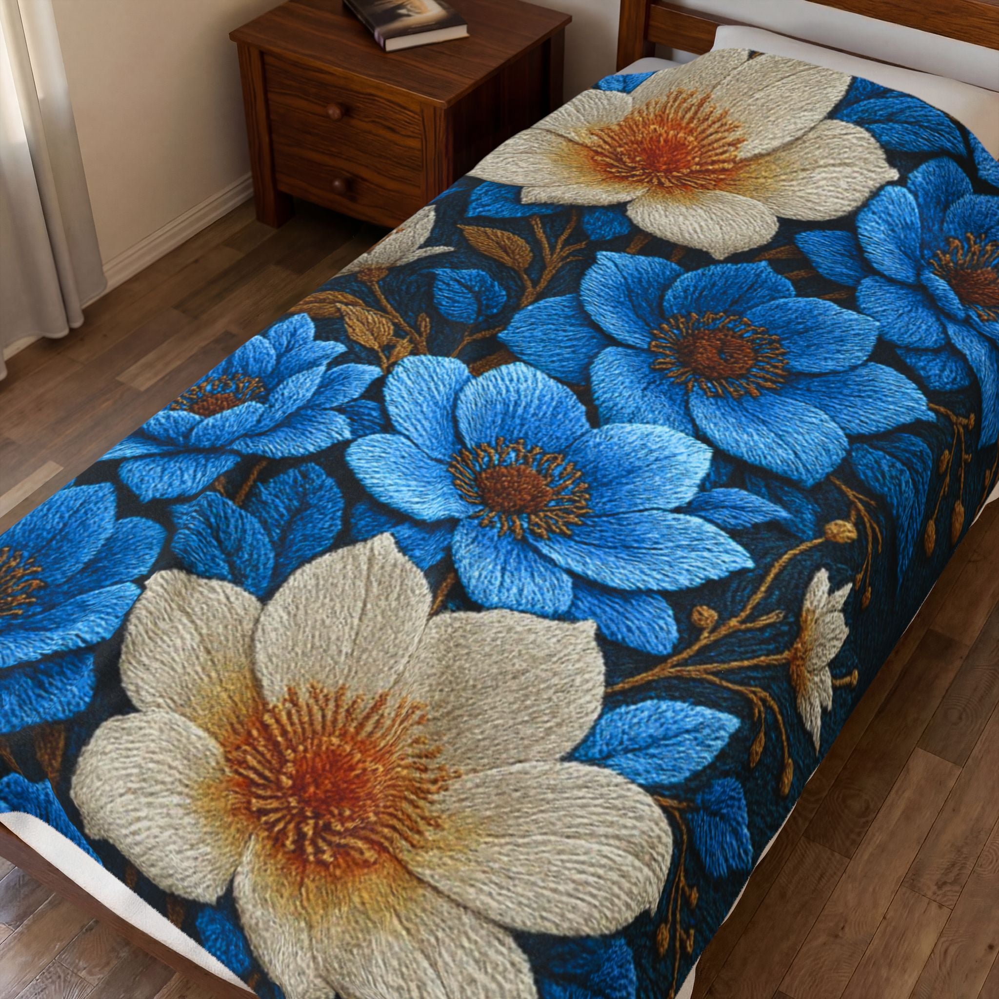 A plush Midnight Symphony blanket with large blue and cream floral patterns spread across a bed in a cozy bedroom setting, showing the rich velveteen texture.