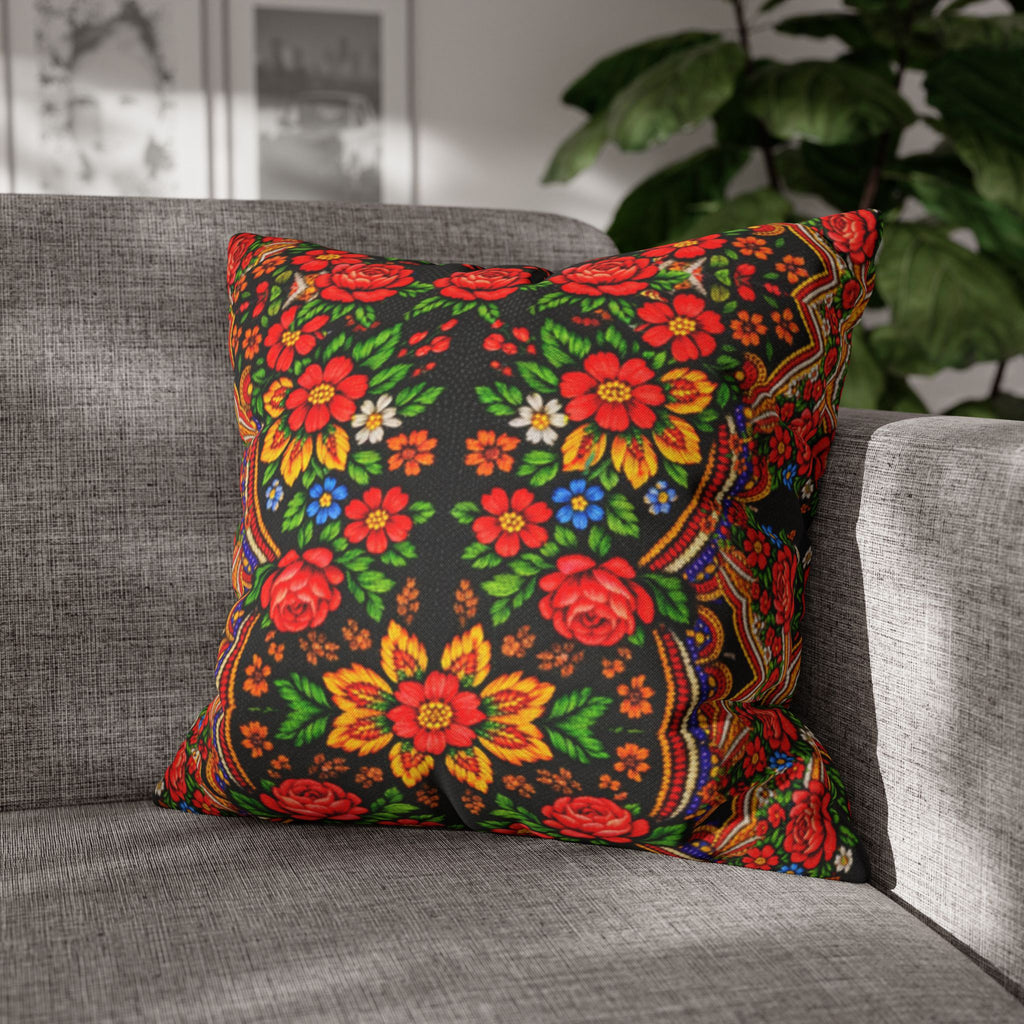 A square decorative pillow named "Mother’s Bloom" with a vibrant red and yellow Ukrainian folk floral pattern on a black background, placed on a grey modern sofa.