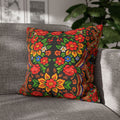 A square decorative pillow named "Mother’s Bloom" with a vibrant red and yellow Ukrainian folk floral pattern on a black background, placed on a grey modern sofa.