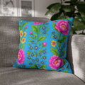 Square decorative pillowcase featuring vertical rows of pink peonies and yellow wildflowers on a bright sky-blue background, resting on a grey fabric sofa.