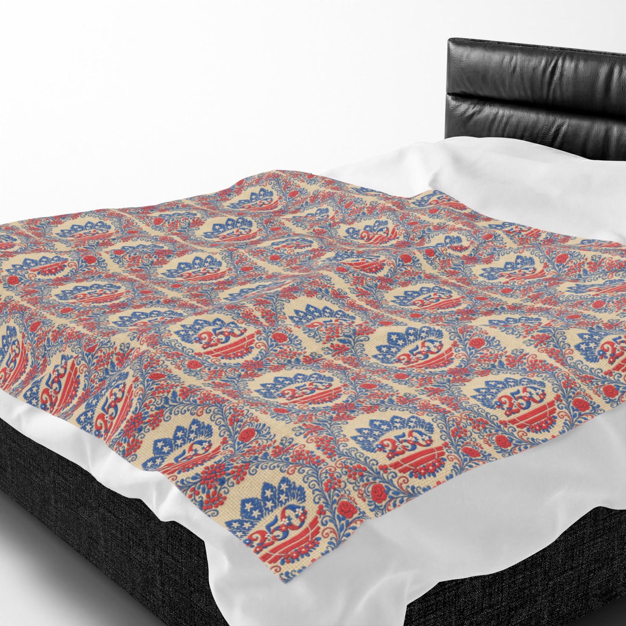 A soft velveteen plush blanket featuring the "Freedom's Garden 250" design. The cream-colored throw shows a repeating pattern of red and blue floral medallions with a "250" anniversary emblem and stars, draped over the edge of a bed with a black headboard.