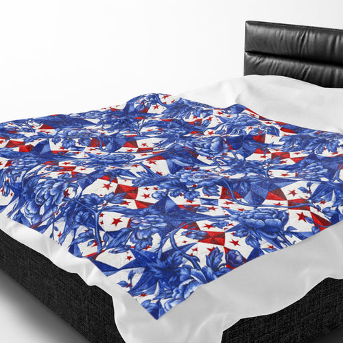 Velveteen plush blanket featuring a blue toile-inspired floral pattern and red patriotic stars from the 250th Collection, draped over a modern black leather bed.