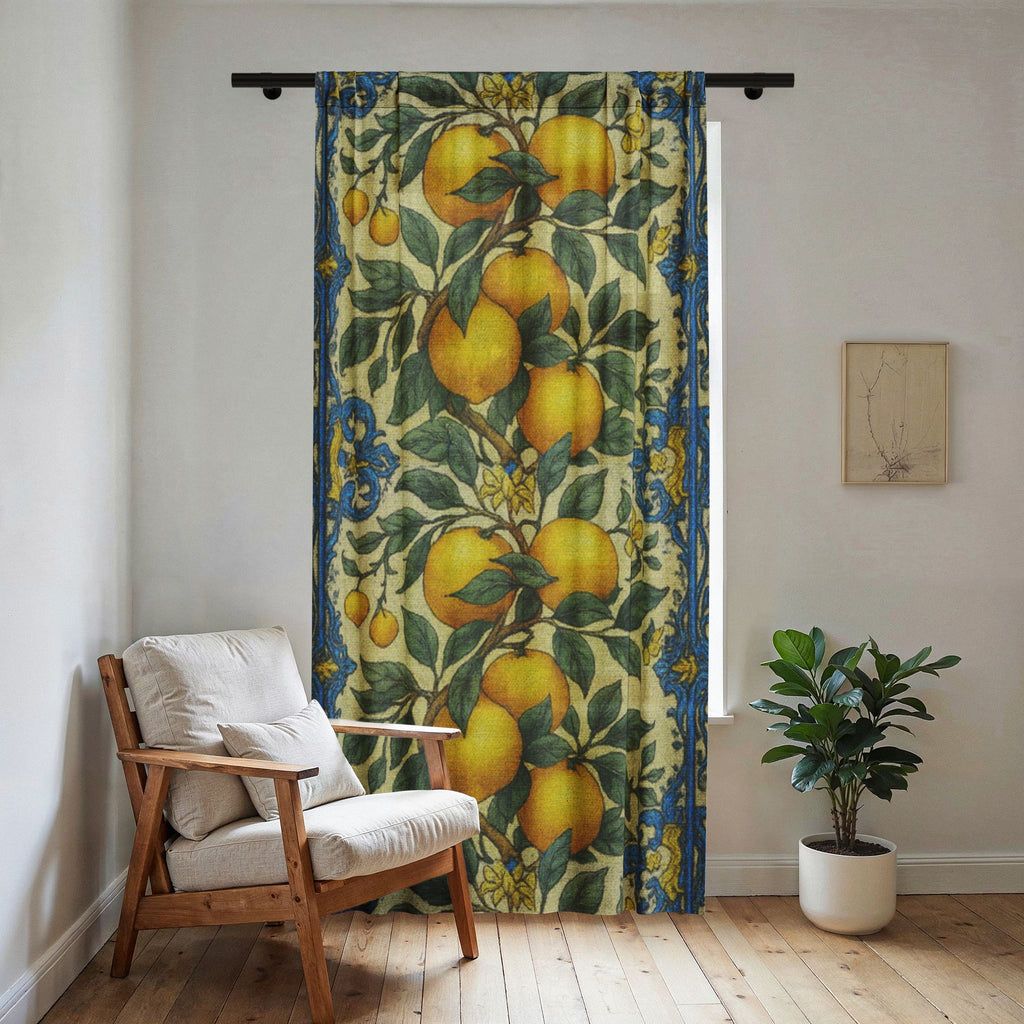 A sheer window curtain with a vintage botanical lemon and orange print and blue borders, hanging in a bright room next to a wooden chair and a green plant.