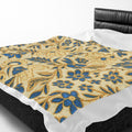 Velveteen plush blanket featuring a William Morris inspired floral pattern with intricate gold flowers and teal blue leaves on a cream background, styled on a modern bed.