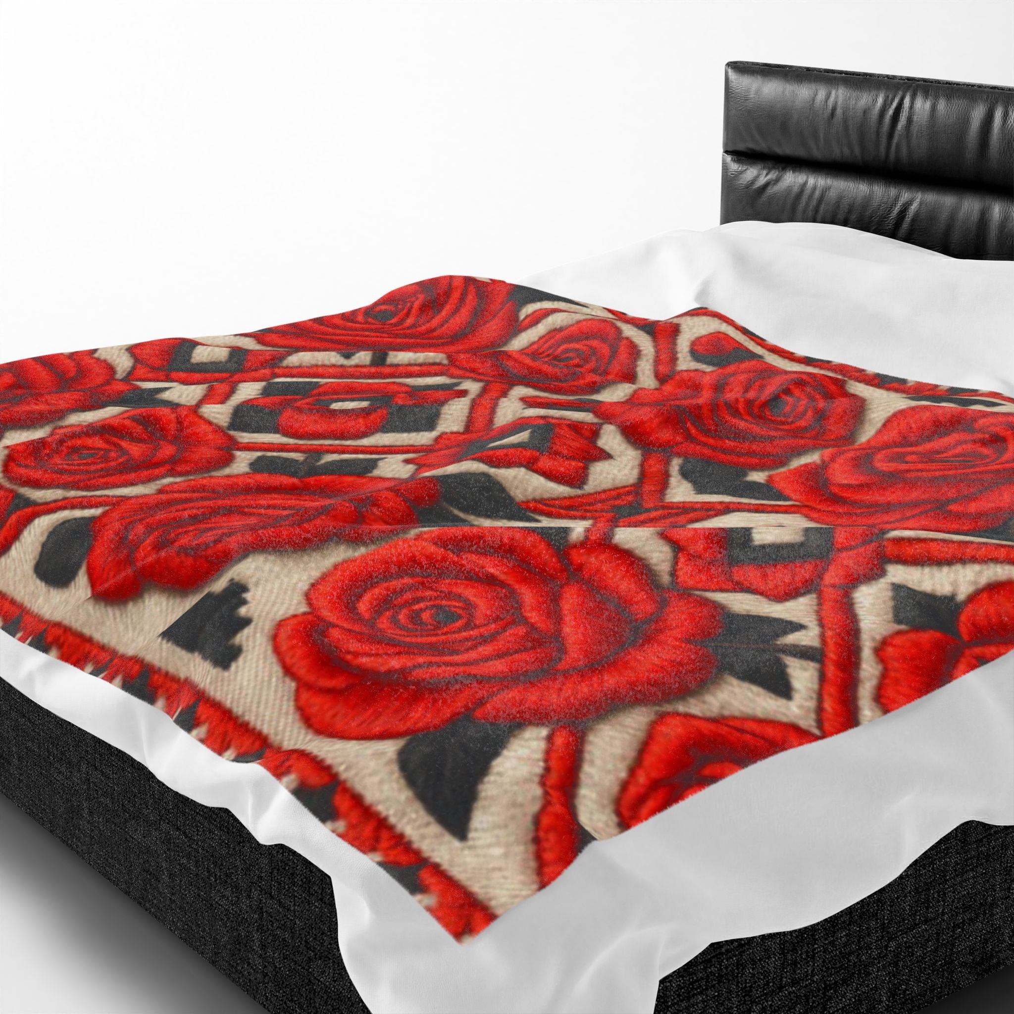 A plush velveteen blanket with a red rose and geometric pattern spread across a white made bed with a black leather headboard.