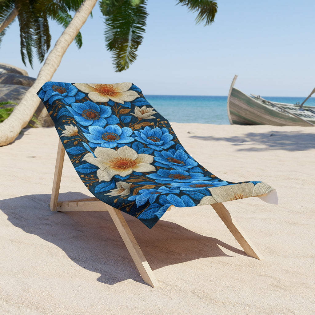 Midnight Symphony beach towel with large blue and cream floral patterns draped over a wooden lounge chair on a tropical sandy beach with palm trees and a boat in the background.