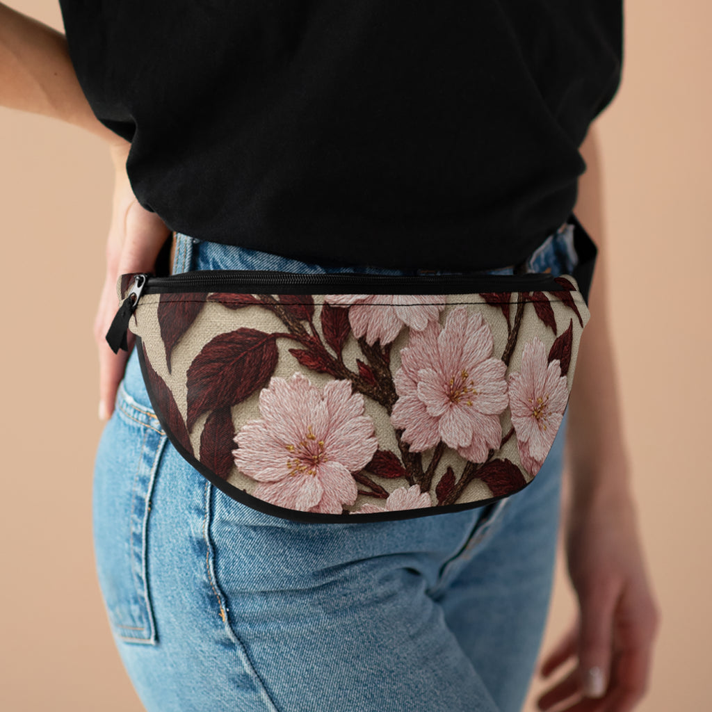 A person wearing the Sakura Noir fanny pack with a pink cherry blossom and dark brown leaf pattern over blue jeans and a black t-shirt.