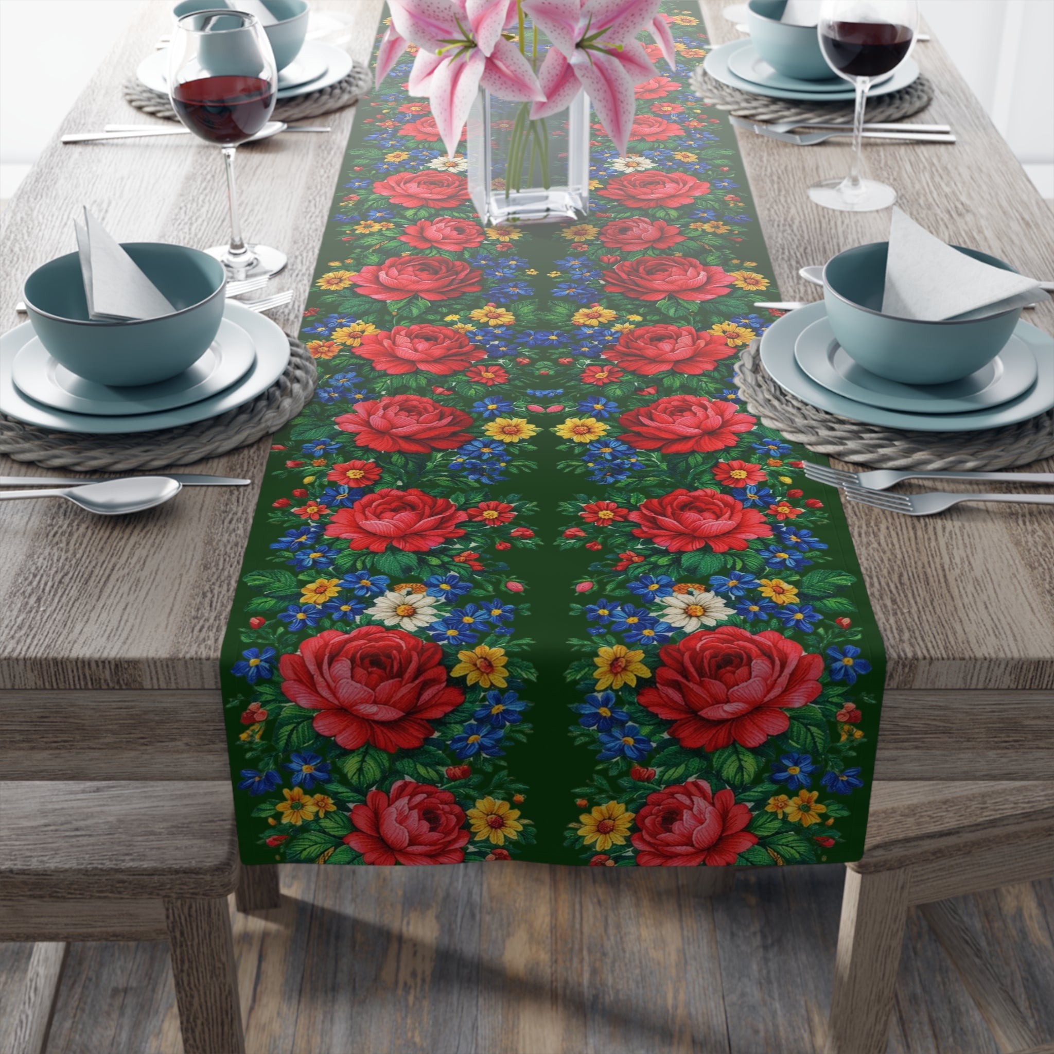 Vintage-style table runner featuring large red roses and small blue and yellow wildflowers on a dark green background, displayed on a wooden dining table with elegant place settings.